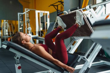 Spor salonunda bacaklar için spor yapan genç bir kadın fitness koçunun görüntüsü.
