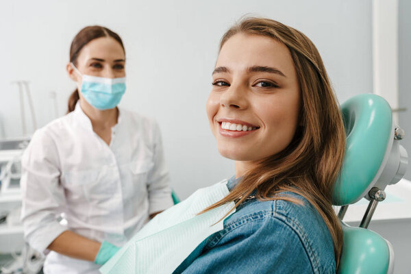 European young woman smiling while sitting in medical chair at dental clinic