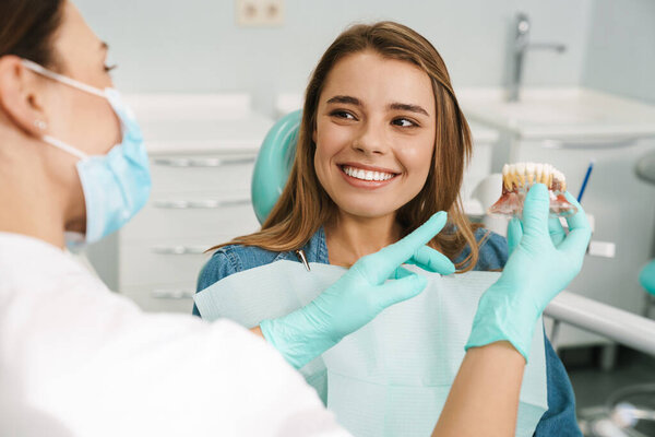 Dentist woman showing teeth imitation to her smiling patient in dental clinic
