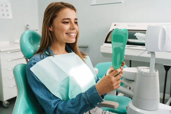 欧洲年轻女子笑着在牙科诊所照镜子 — 图库照片