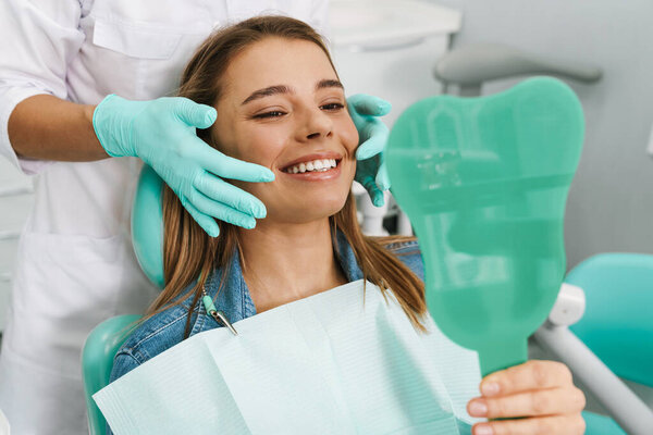 European young woman smiling while looking at mirror in dental clinic