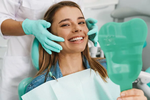 欧洲年轻女子笑着在牙科诊所照镜子 — 图库照片