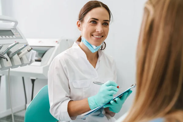 歯医者で患者と仕事をしながら笑顔ヨーロッパの中堅歯科医の女性 — ストック写真