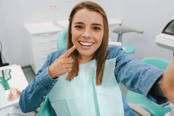 在牙科诊所里 快乐的女人一边微笑一边指指点点自己的微笑 — 图库照片
