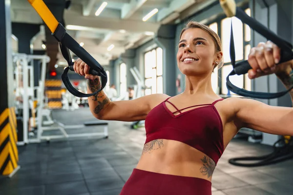 在健身房锻炼的同时 带着健身器械做运动的女运动员的微笑 — 图库照片