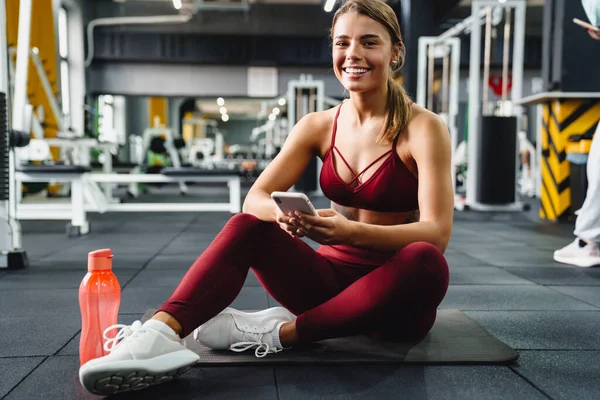 Foto Alegre Joven Positiva Entrenador Fitness Utilizando Teléfono Móvil Gimnasio —  Fotos de Stock