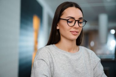 Gözlüklü mutlu genç kadın evde poz verirken gülümsüyor.