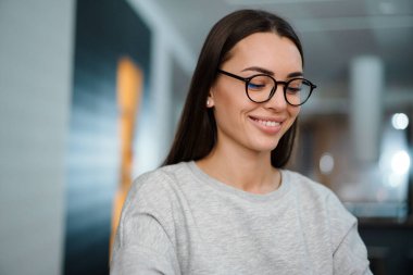 Gözlüklü mutlu genç kadın evde poz verirken gülümsüyor.