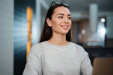 Evde dizüstü bilgisayarla çalışırken gülümseyen gözlüklü mutlu genç kadın.