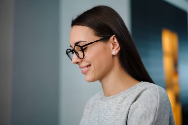 Gözlüklü mutlu genç kadın evde poz verirken gülümsüyor.