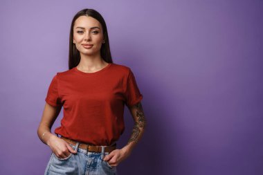 Sevinçli esmer kız gülümsüyor ve mor arka planda izole edilmiş kameraya bakıyor.