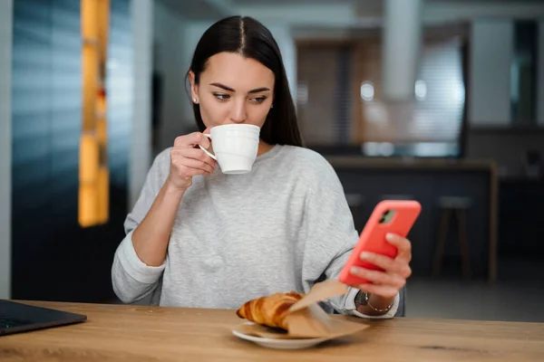 Fókuszált Fiatal Mobiltelefon Használata Közben Kávézás Croissant Otthon — Stock Fotó