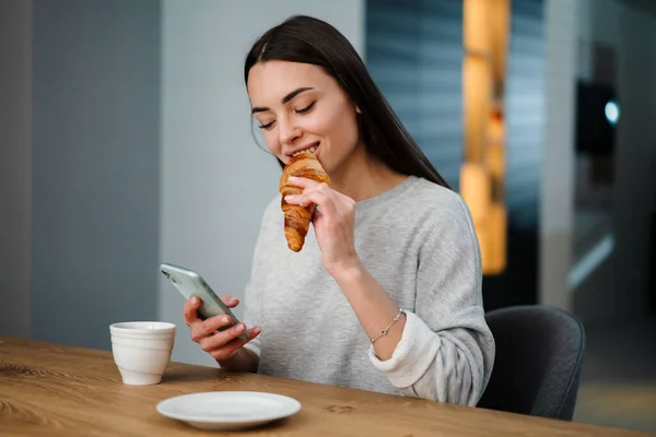 Boldog Fiatal Használja Mobiltelefon Miközben Iszik Kávét Croissant Otthon — Stock Fotó
