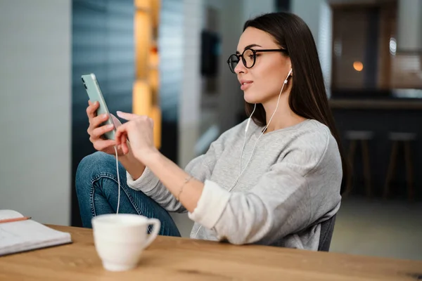 Pleased Young Woman Listening Music Earphones Mobile Phone While Sitting — 图库照片