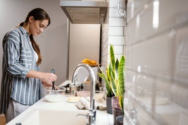 Gülümseyen ve ev mutfağında krep hamuru yapan güzel bir kadın.