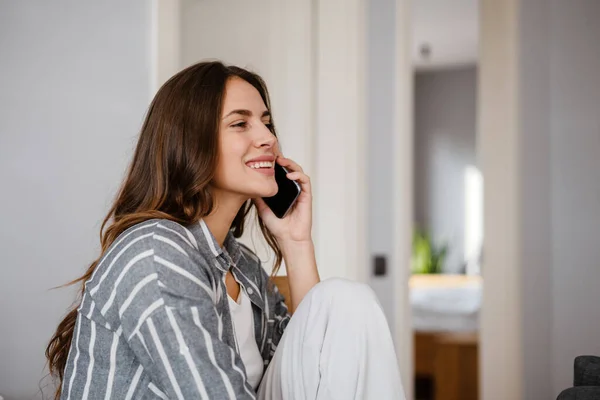 Glückliche Schöne Frau Lächelt Und Telefoniert Während Sie Hause Sitzt — Stockfoto