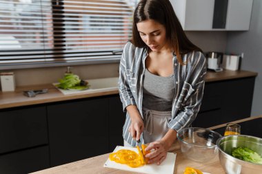 Büyüleyici odaklı kadın evde rahat mutfakta salata hazırlıyor.