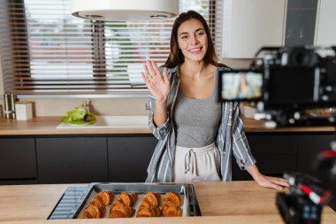 Evdeki rahat mutfakta el sallayan ve kruvasan pişiren mutlu kadının kamera görüntüleri.