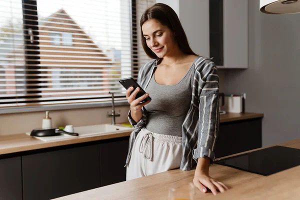 Обаятельная Счастливая Женщина Улыбается Пользуясь Мобильным Телефоном Уютной Домашней Кухне — стоковое фото