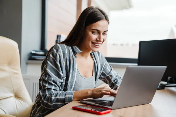 Sjarmerende Lykkelig Kvinne Som Smiler Mens Hun Jobber Med Laptopen – stockfoto