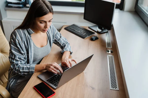 Encantadora Mulher Focada Trabalhando Com Laptop Enquanto Senta Mesa Casa — Fotografia de Stock