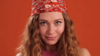 Kafasında bandana olan kıvırcık saçlı kadının turuncu stüdyodaki kameraya yakından bakışıyla.