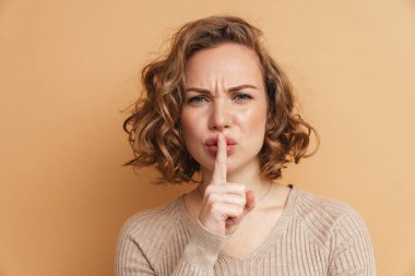 Kızıl saçlı hoşnutsuz kadın bej arka planda izole edilmiş kameraya sessiz jest yapıyor.