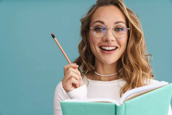 Uśmiechnięta Młoda Kobieta Okularach Trzyma Ołówek Książki Tle Niebieskiej Ściany — Zdjęcie stockowe