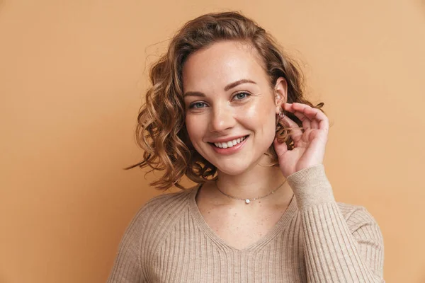 Young ginger woman with wavy hair smiling and looking at camera isolated over beige background