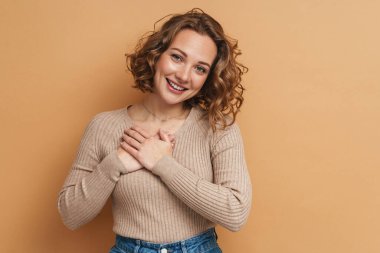 Bej arka planda el ele tutuşurken gülümseyen genç kızıl kadın.