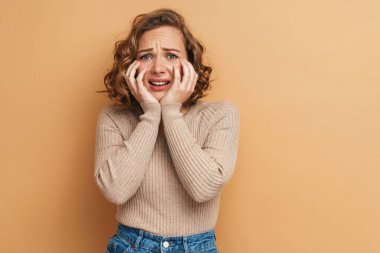 Genç kızıldan korkan kadın bej arka planda izole edilmiş kameraya bakıyor.