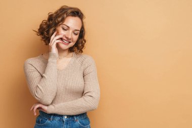 Kızıl saçlı genç kadın bej arka planda izole edilmiş kameraya gülüyor.