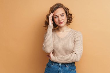 Alnına değen baş ağrısı olan kızıl saçlı genç bir kadın bej arka planda izole edilmiş.