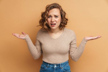 Dalgalı saçlı, kızıl saçlı genç kadın bej arka planda izole edilmiş kopyalama alanı tutuyor.
