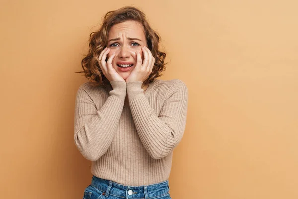 Young ginger scared woman frowning and looking at camera isolated over beige background