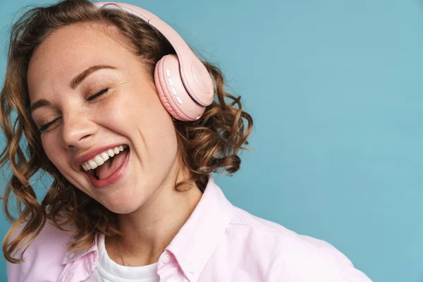 Junge Ingwerfrau Lacht Während Sie Mit Kopfhörern Auf Blauem Hintergrund — Stockfoto