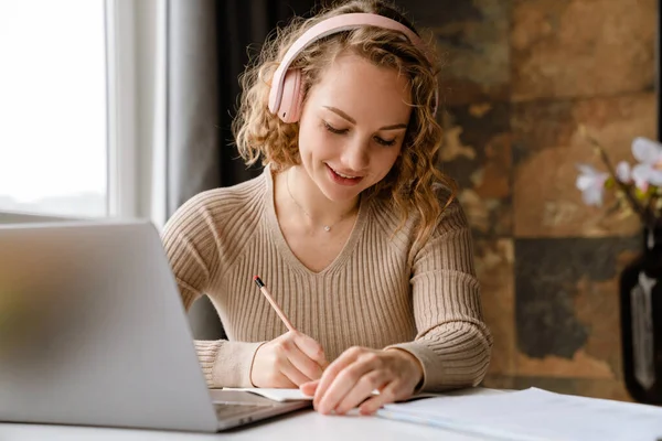 Mujer Joven Auriculares Anotando Notas Mientras Trabaja Con Ordenador Portátil — Foto de Stock
