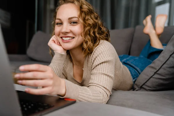 Hvid Blondine Kvinde Smilende Bruger Bærbar Computer Mens Ligger Sofaen - Stock-foto