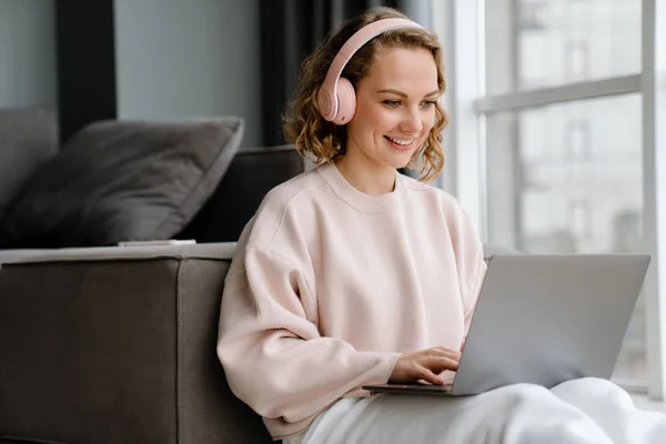 Kulaklıklı Beyaz Kadın Evde Otururken Dizüstü Bilgisayar Kullanıyor — Stok fotoğraf