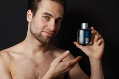 Üstsüz beyaz adam gülümserken mavi duvarın üzerinde izole edilmiş kolonya gösteriyor.