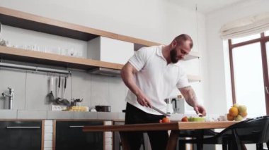 A calm muscular man is cooking while cutting fruits standing in the kitchen at home