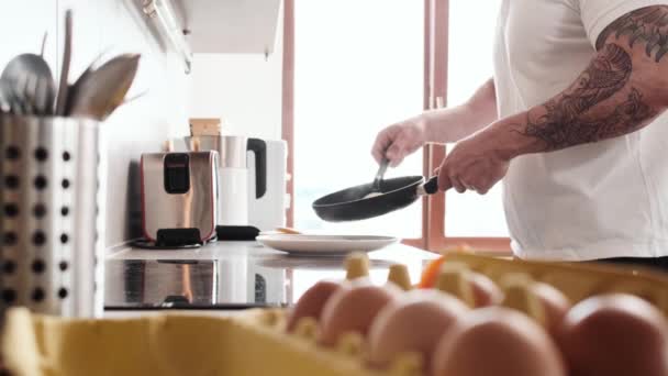 入れ墨のハンサムな男のクロップドビューは 自宅でキッチンに立って朝食を調理しています — ストック動画