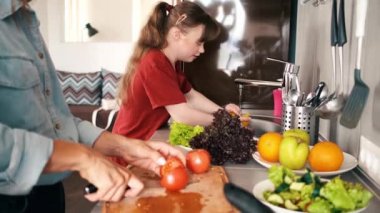 A positive young girl with down syndrome is making salad with her mother is helping her at home