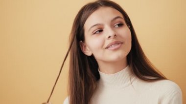Çekici, utangaç bir kadının yakın plan görüntüsü bir şey hayal ediyor ve stüdyodaki bej duvarın üzerinde izole bir şekilde duran kameraya bakıyor.