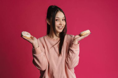 Mor duvarda izole edilmiş çöreklerle poz verirken gülümseyen Asyalı esmer kadın.