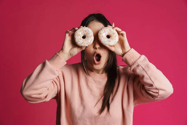 快乐的年轻女子在粉红的墙壁背景上摆着甜甜圈的姿势 — 图库照片