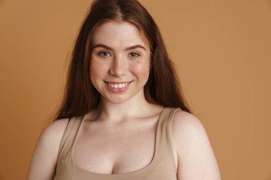 Gülümseyen genç ve iri yarı kadın bej arka planda poz veriyor.