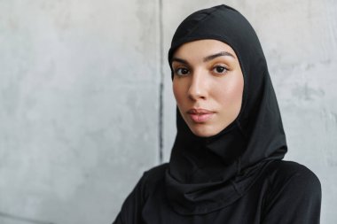 Başörtülü genç Müslüman kadın içeride poz veriyor ve kameraya bakıyor.