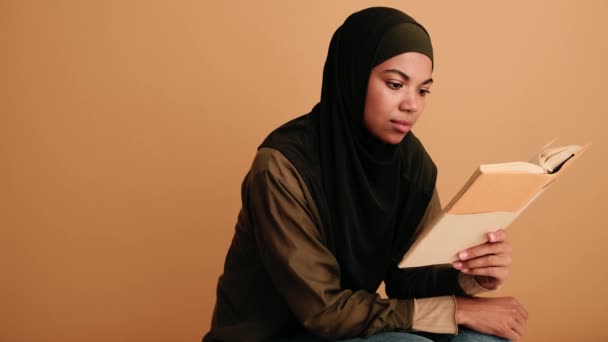 一位专心致志的阿拉伯妇女孤零零地坐在米色的背景下看书 — 图库视频影像