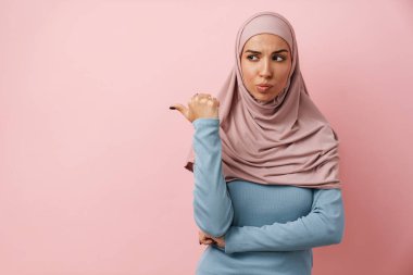 Telif alanını gösteren pembe tesettürlü üzgün bir müslüman kadın pembe stüdyoda alnını kırıştırıyor.